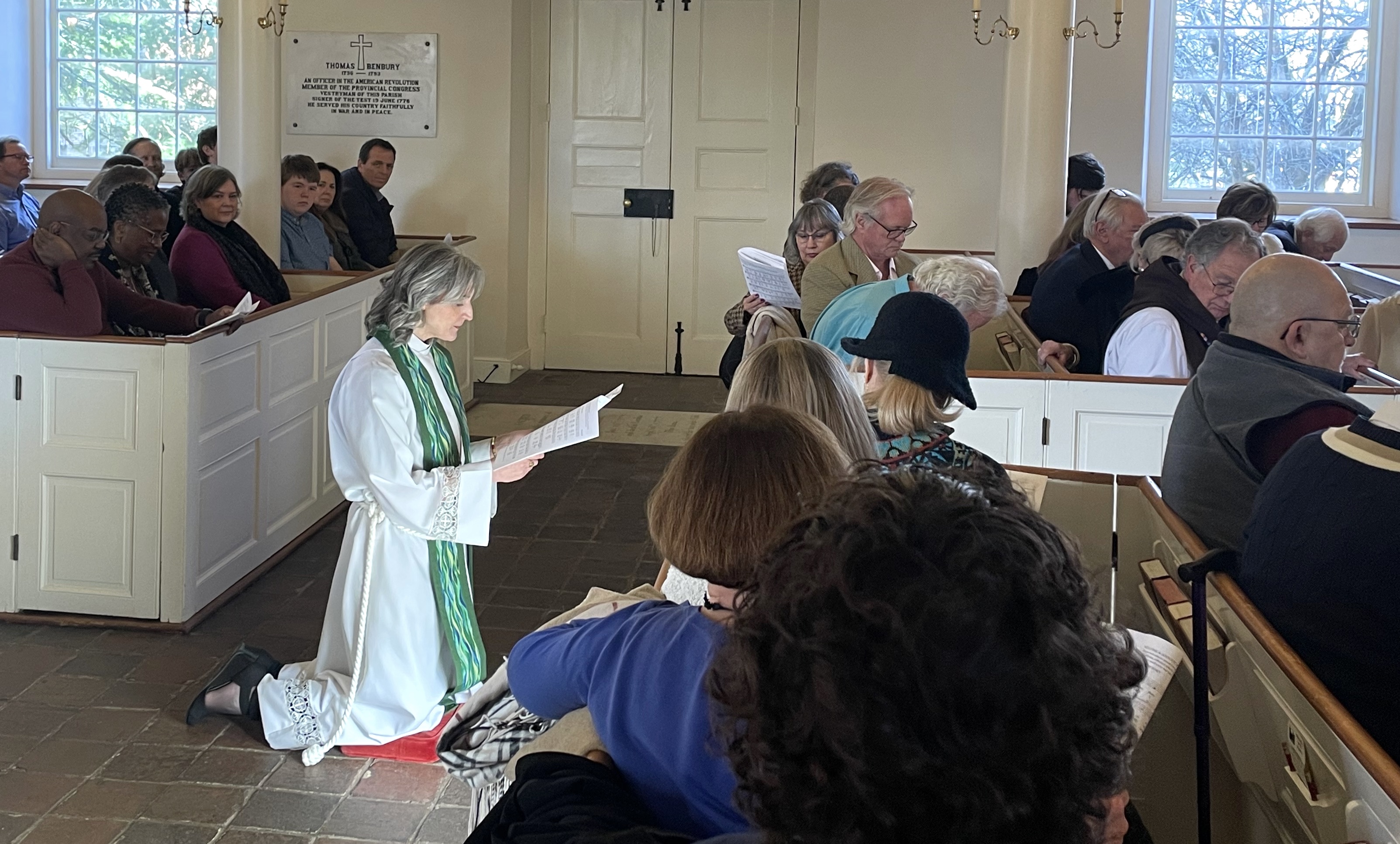 woman kneels while others sit in pews.