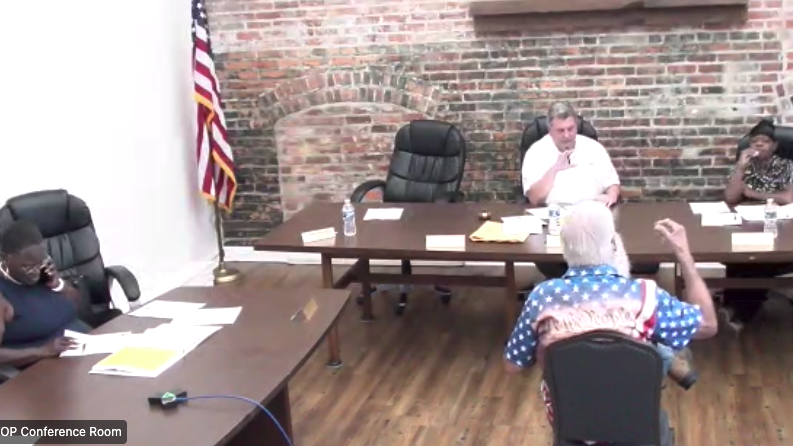 People sit at tables while a man in a chair gestures.