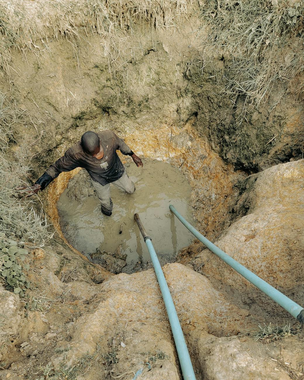 man working in muddy excavation site with pipes